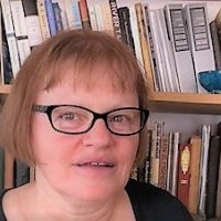 a white woman with glasses standing in front of books on shelves