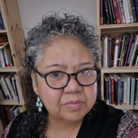 a Boricua woman with glasses with two bookshelves in the background